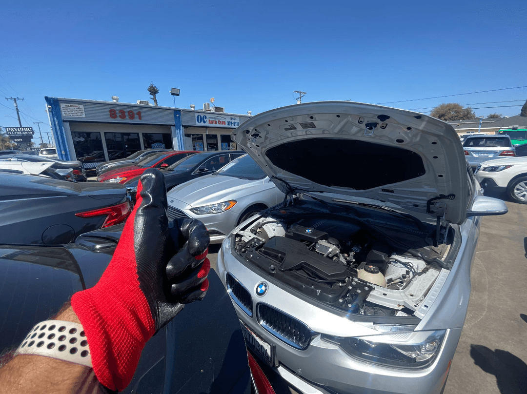 picture of a mechanic with his thumb up in the air in front of a car